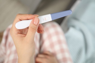 Woman holding positive pregnancy test indoors, closeup view