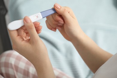 Woman holding negative pregnancy test indoors, closeup view