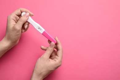 Woman holding pregnancy test on pink background, top view. Space for text