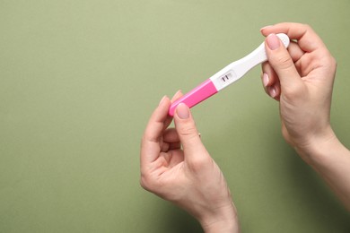 Photo of Woman holding pregnancy test on olive background, top view. Space for text