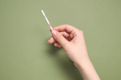 Photo of Woman holding pregnancy test on olive background, top view. Space for text