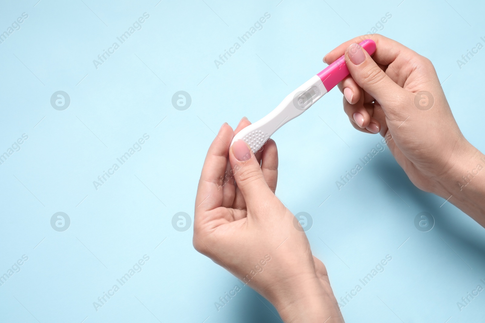 Photo of Woman holding pregnancy test on light blue background, closeup. Space for text