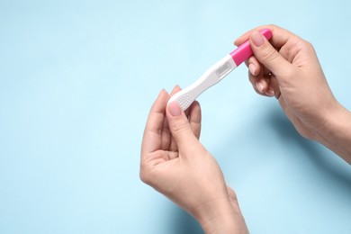 Woman holding pregnancy test on light blue background, closeup. Space for text