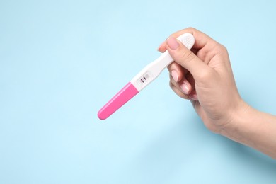 Woman holding pregnancy test on light blue background, closeup. Space for text