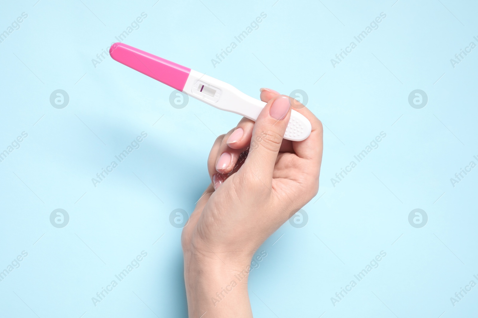 Photo of Woman holding pregnancy test on light blue background, closeup