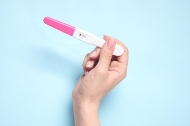 Photo of Woman holding pregnancy test on light blue background, closeup