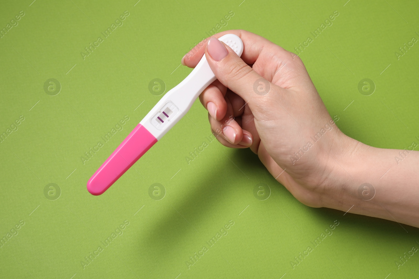 Photo of Woman holding pregnancy test on green background, closeup