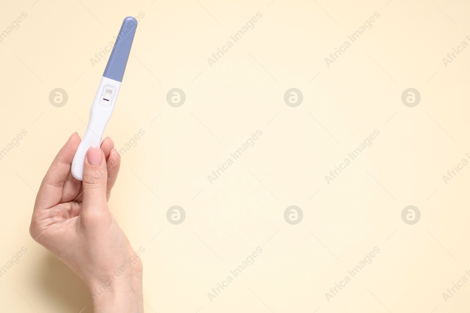 Photo of Woman holding pregnancy test on beige background, top view. Space for text