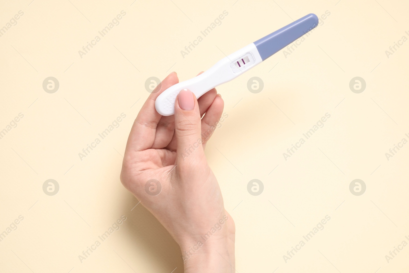 Photo of Woman holding pregnancy test on beige background, top view