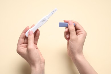 Photo of Woman holding pregnancy test on beige background, top view