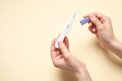 Woman holding pregnancy test on beige background, closeup. Space for text