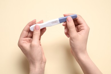 Woman holding pregnancy test on beige background, closeup