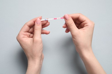 Photo of Woman holding pregnancy test on light grey background, top view