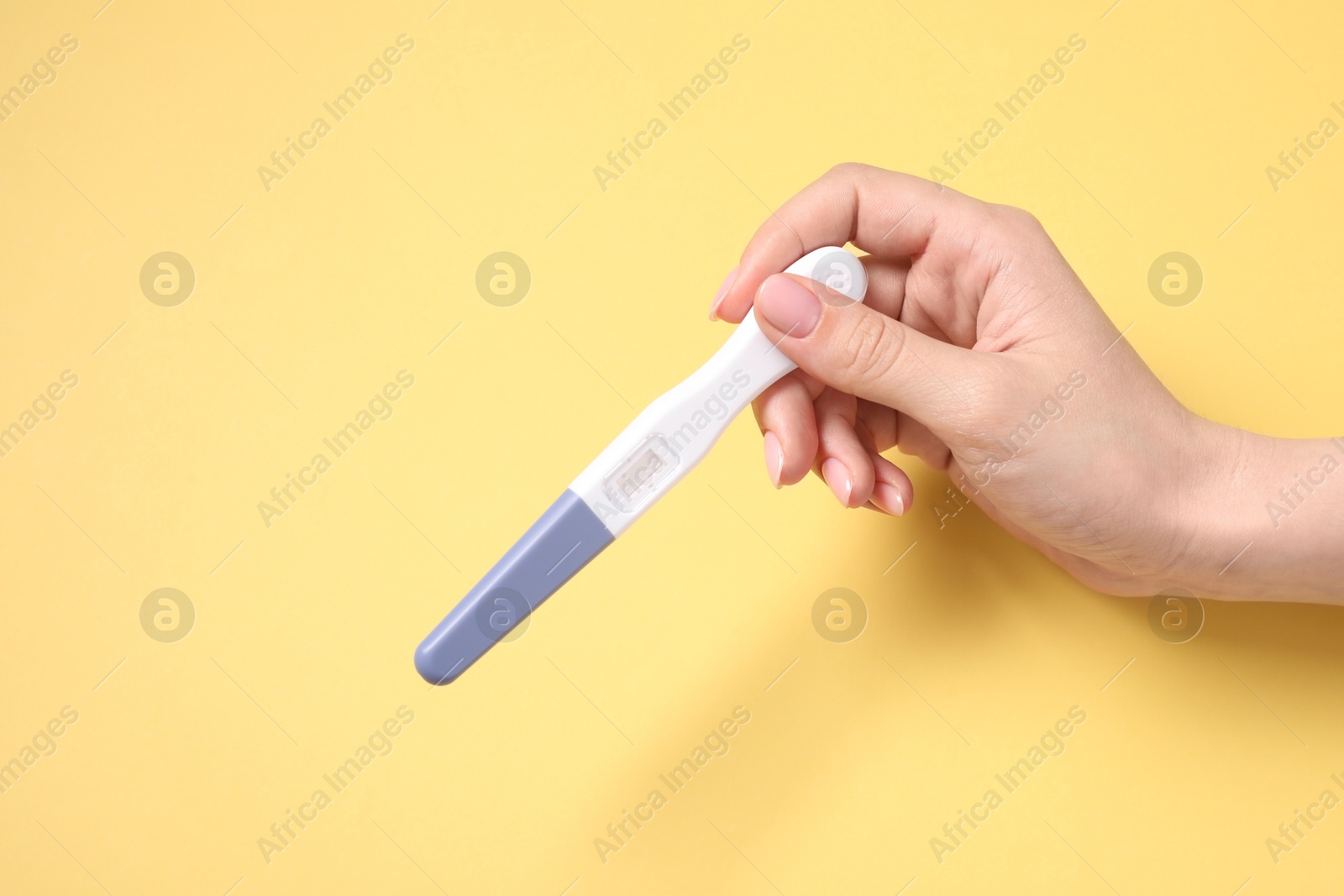 Photo of Woman holding pregnancy test on yellow background, top view