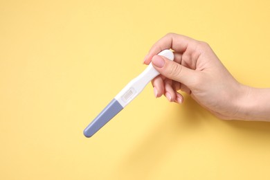 Photo of Woman holding pregnancy test on yellow background, top view