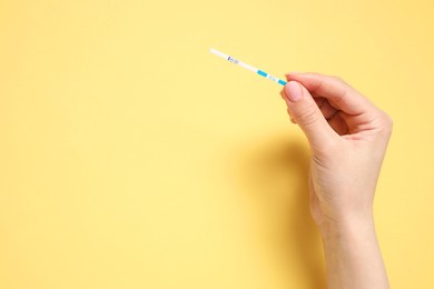 Photo of Woman holding pregnancy test on yellow background, top view. Space for text