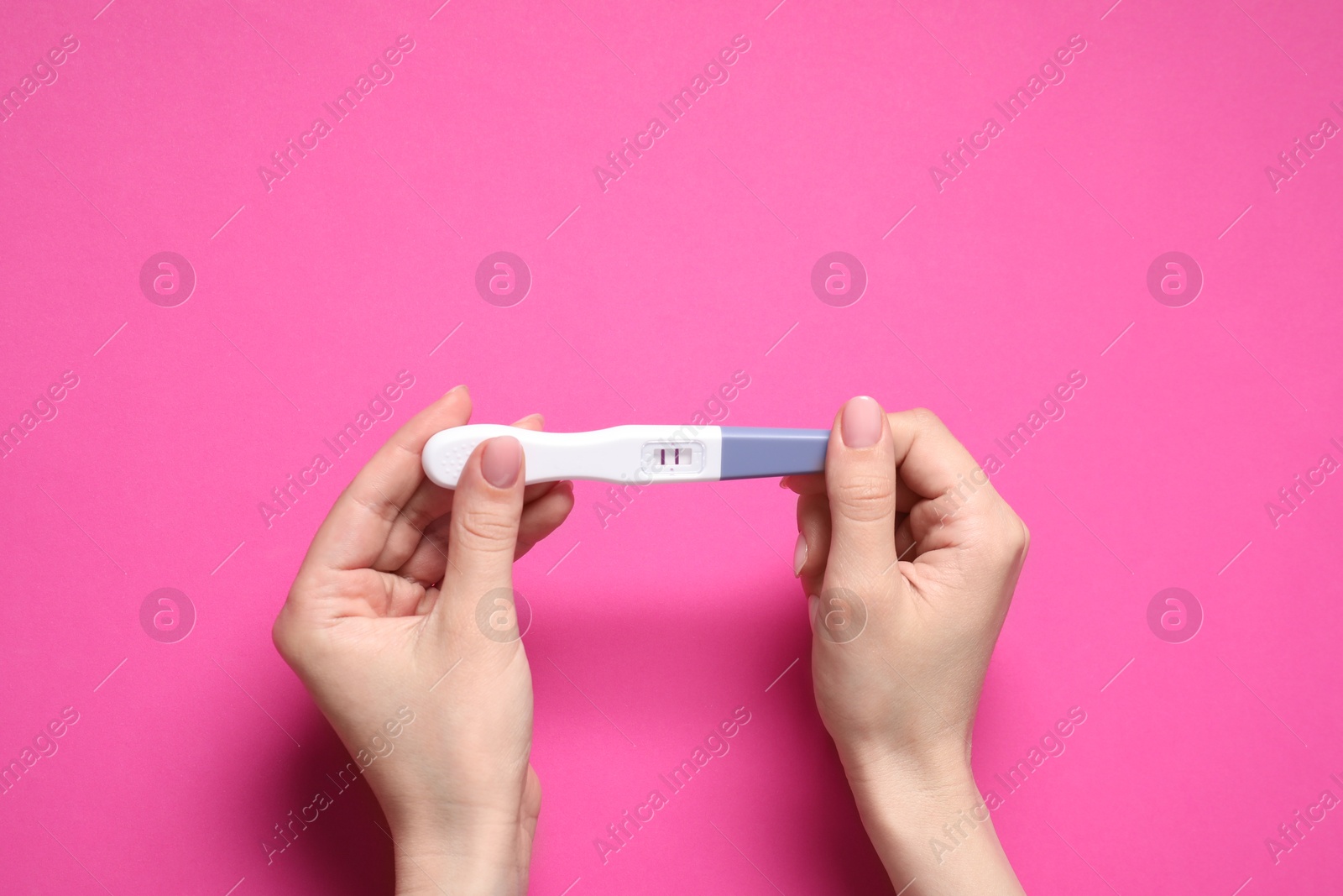 Photo of Woman holding pregnancy test on pink background, top view