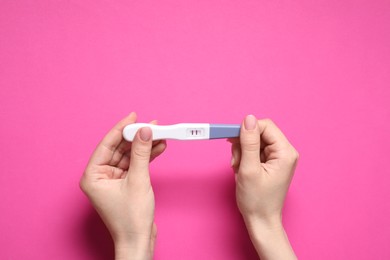 Woman holding pregnancy test on pink background, top view