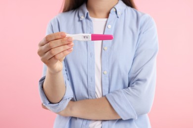 Photo of Woman holding pregnancy test on pink background, closeup