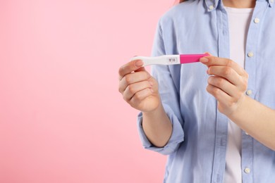 Photo of Woman holding pregnancy test on pink background, closeup. Space for text