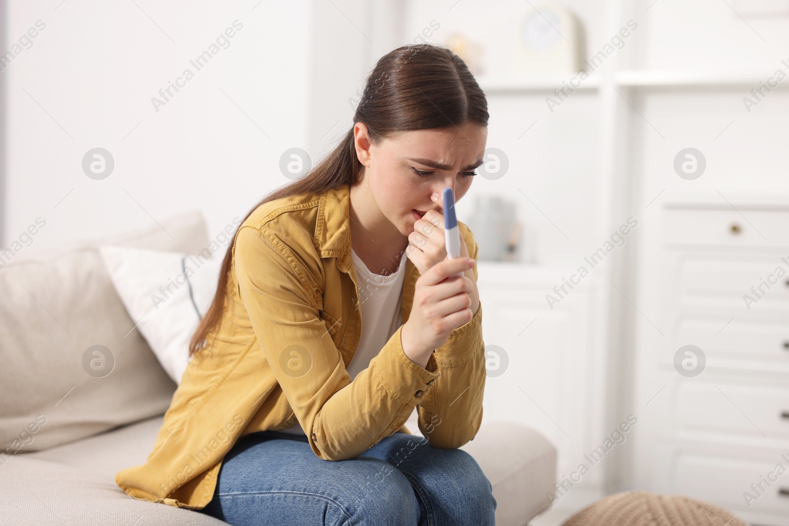 Photo of Sad woman holding pregnancy test on sofa indoors, space for text