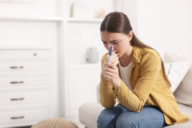 Sad woman holding pregnancy test on sofa indoors, space for text