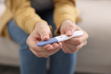 Photo of Woman holding pregnancy test on sofa indoors, closeup