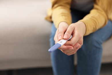 Photo of Woman holding pregnancy test on sofa indoors, closeup. Space for text