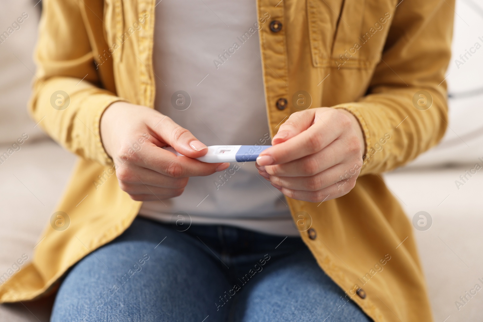 Photo of Woman holding pregnancy test on sofa indoors, closeup