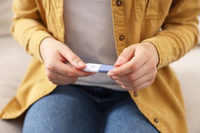 Woman holding pregnancy test on sofa indoors, closeup