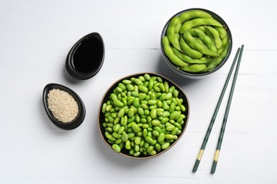 Fresh edamame soybeans, pods, soy sauce and seeds on white wooden table, flat lay