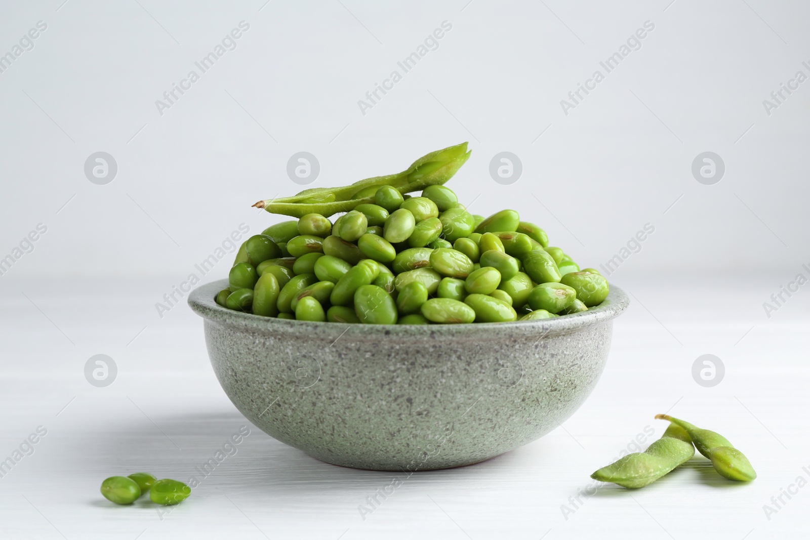 Photo of Fresh edamame soybeans in bowl and pods on white wooden table, closeup