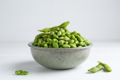 Fresh edamame soybeans in bowl and pods on white wooden table, closeup