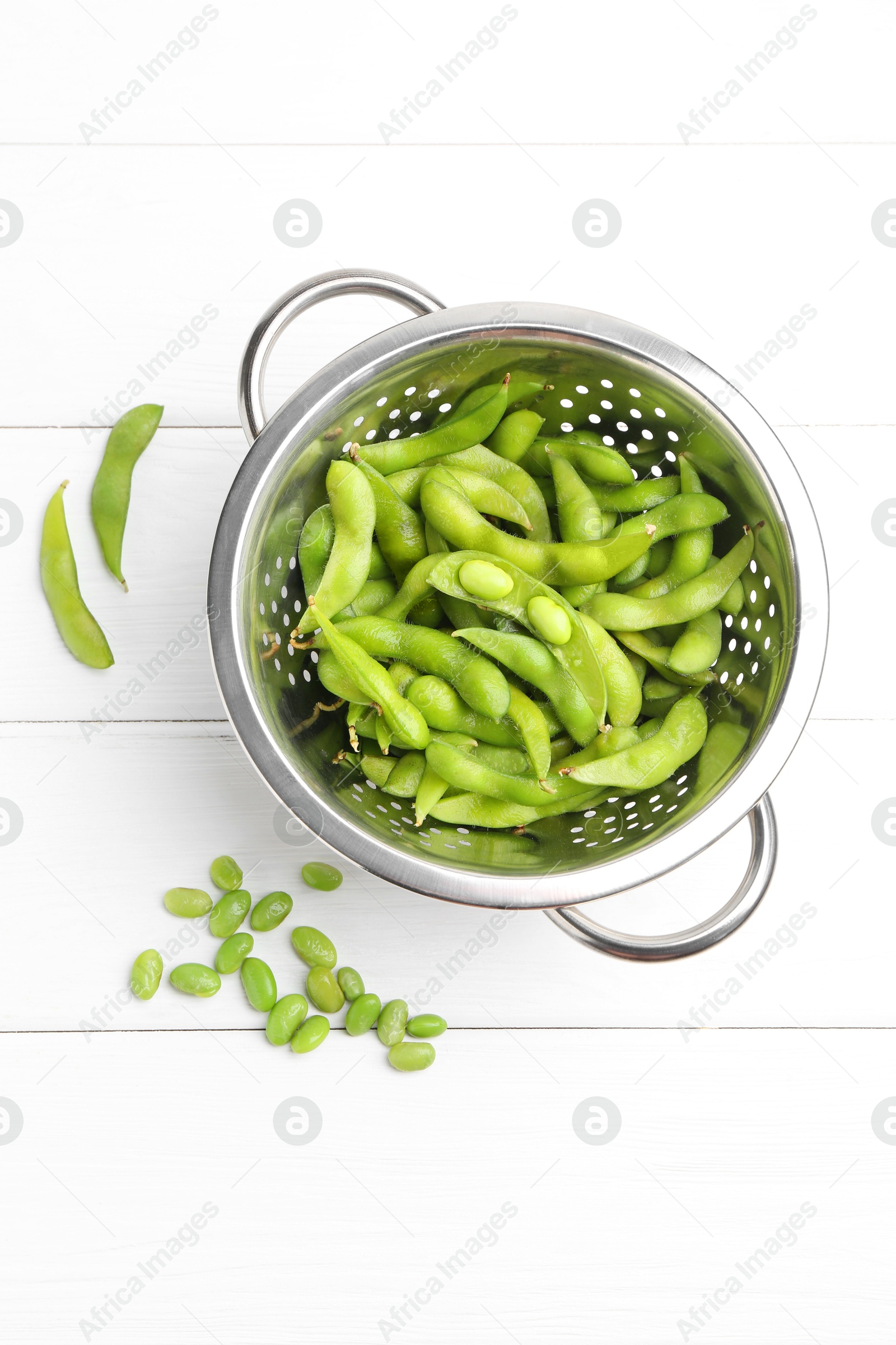 Photo of Fresh edamame pods and soybeans in colander on white wooden table, flat lay