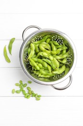 Fresh edamame pods and soybeans in colander on white wooden table, flat lay