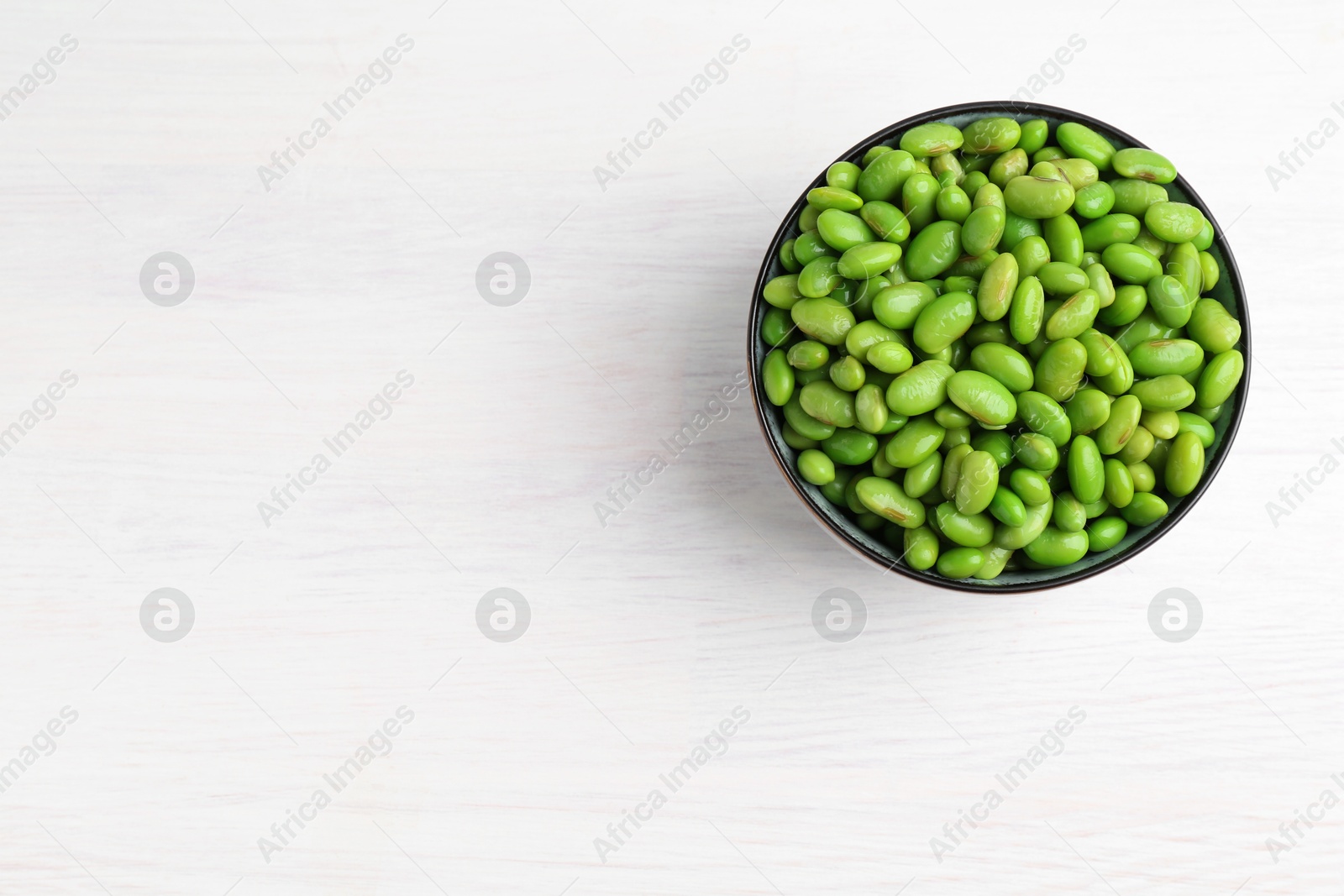 Photo of Fresh edamame soybeans in bowl on white wooden table, top view. Space for text