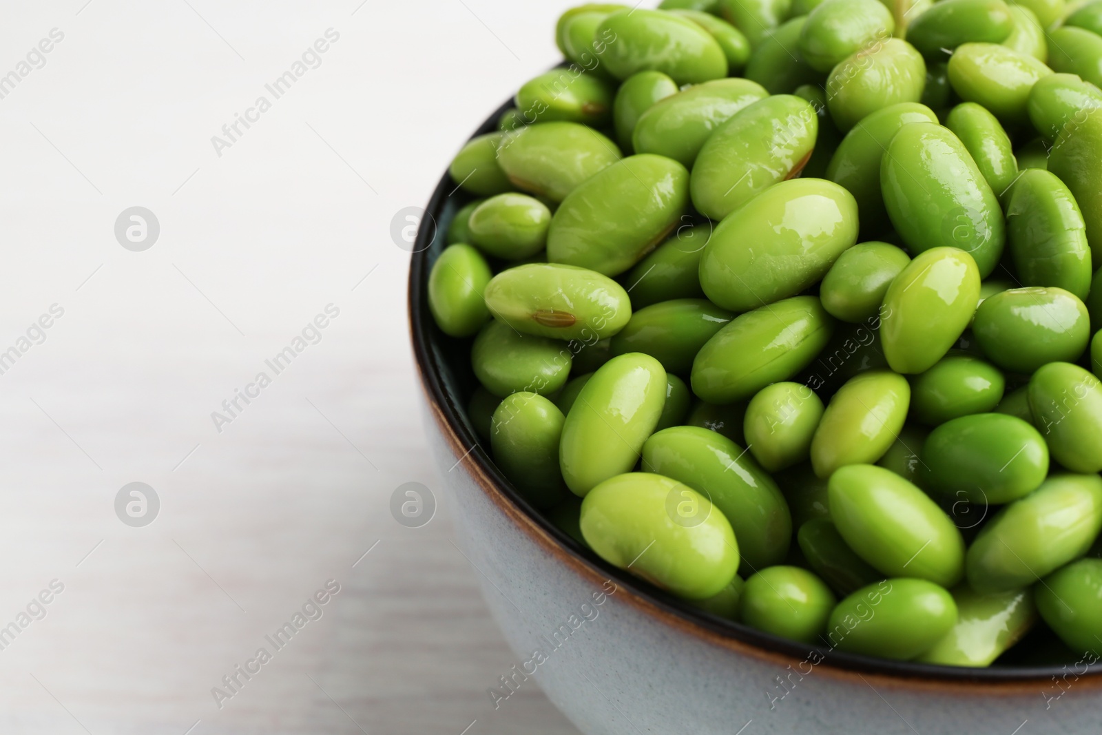 Photo of Fresh edamame soybeans in bowl on white wooden table, closeup. Space for text