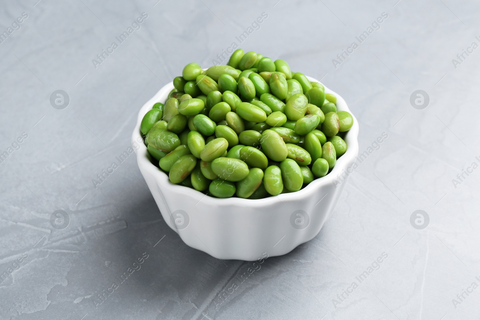 Photo of Fresh edamame soybeans in bowl on grey textured table, closeup