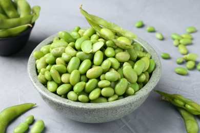 Fresh edamame soybeans in bowl and pods on grey textured table, closeup