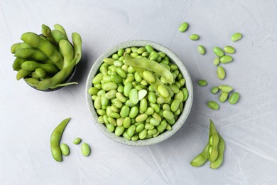 Photo of Fresh edamame soybeans in bowl and pods on grey textured table, flat lay