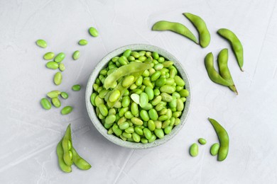 Photo of Fresh edamame soybeans in bowl and pods on grey textured table, flat lay