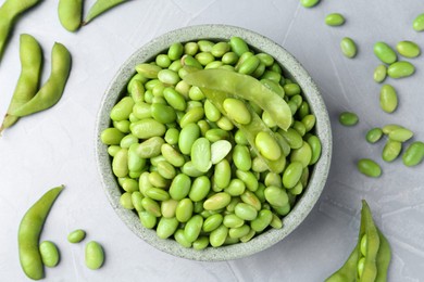 Photo of Fresh edamame soybeans in bowl and pods on grey textured table, flat lay