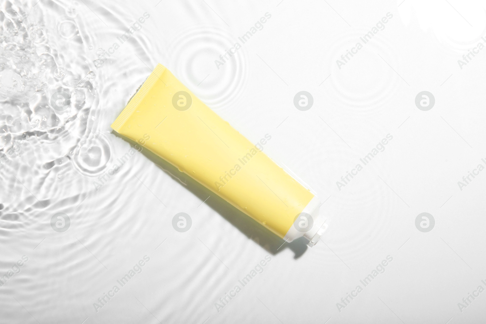 Photo of Cosmetic product. Tube with cream in water on light background, top view