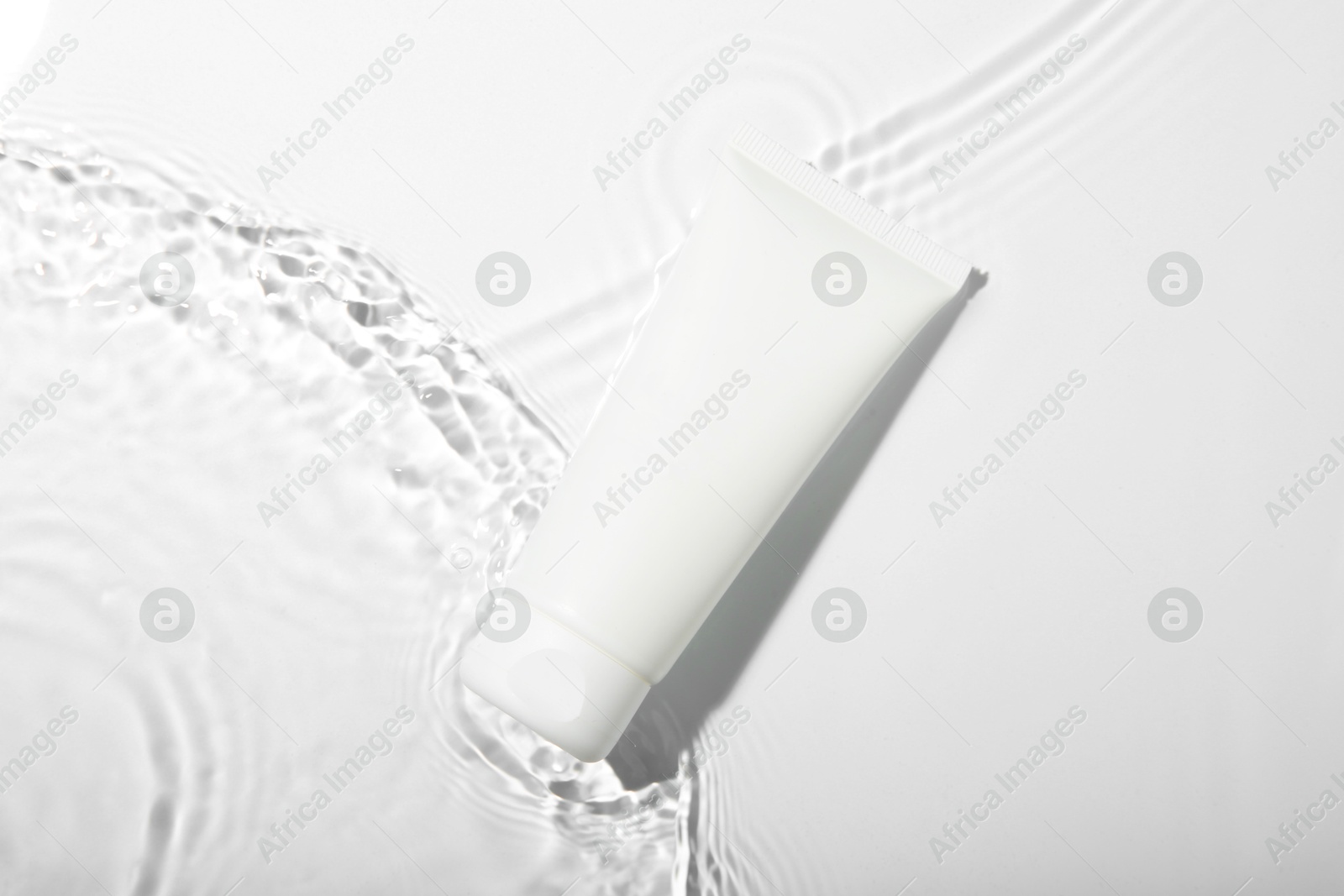 Photo of Cosmetic product. Tube with cream in water on light background, top view