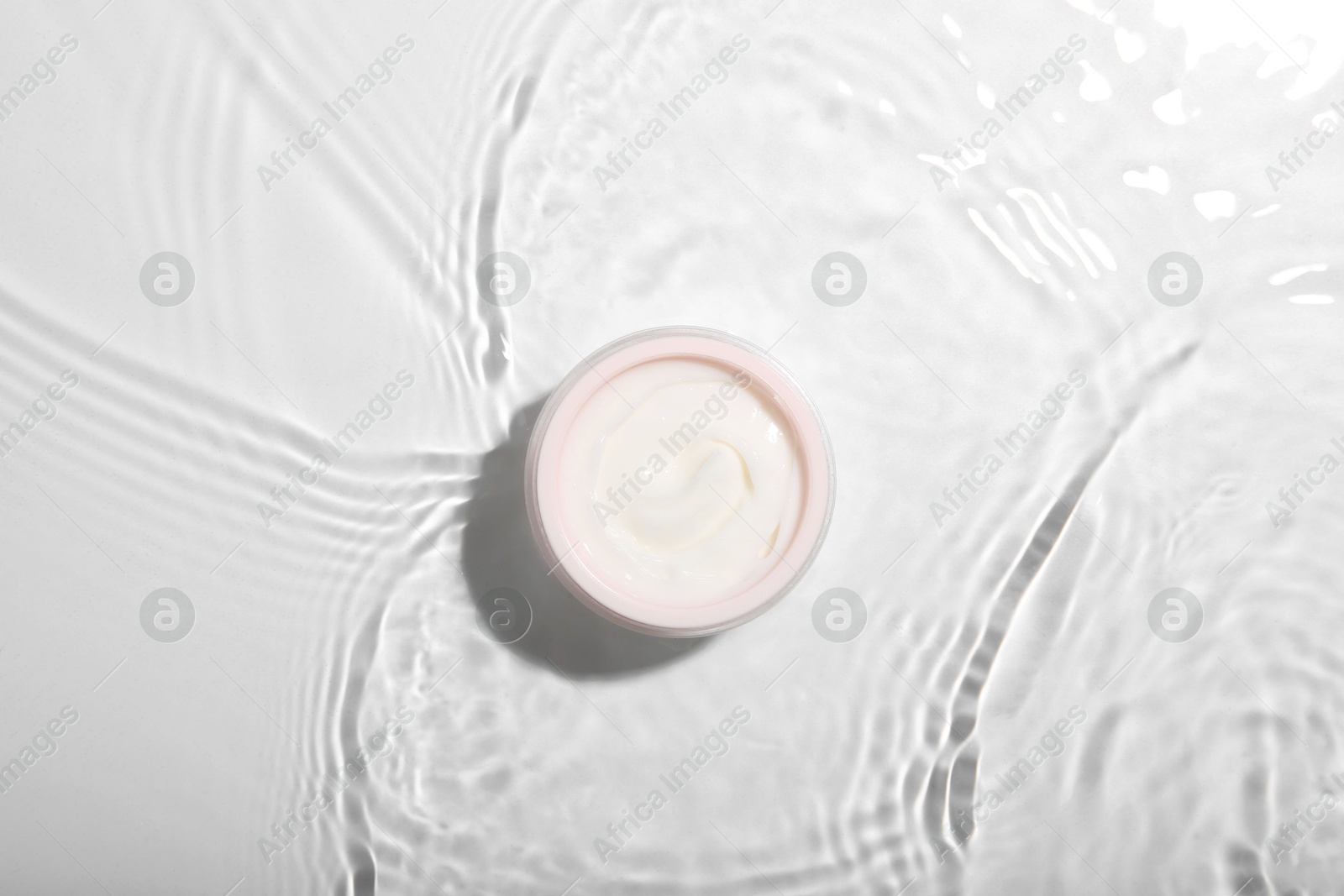 Photo of Cosmetic product. Jar with cream in water on light background, top view