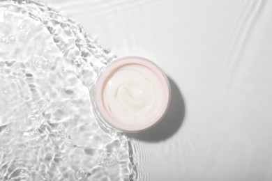 Photo of Cosmetic product. Jar with cream in water on light background, top view