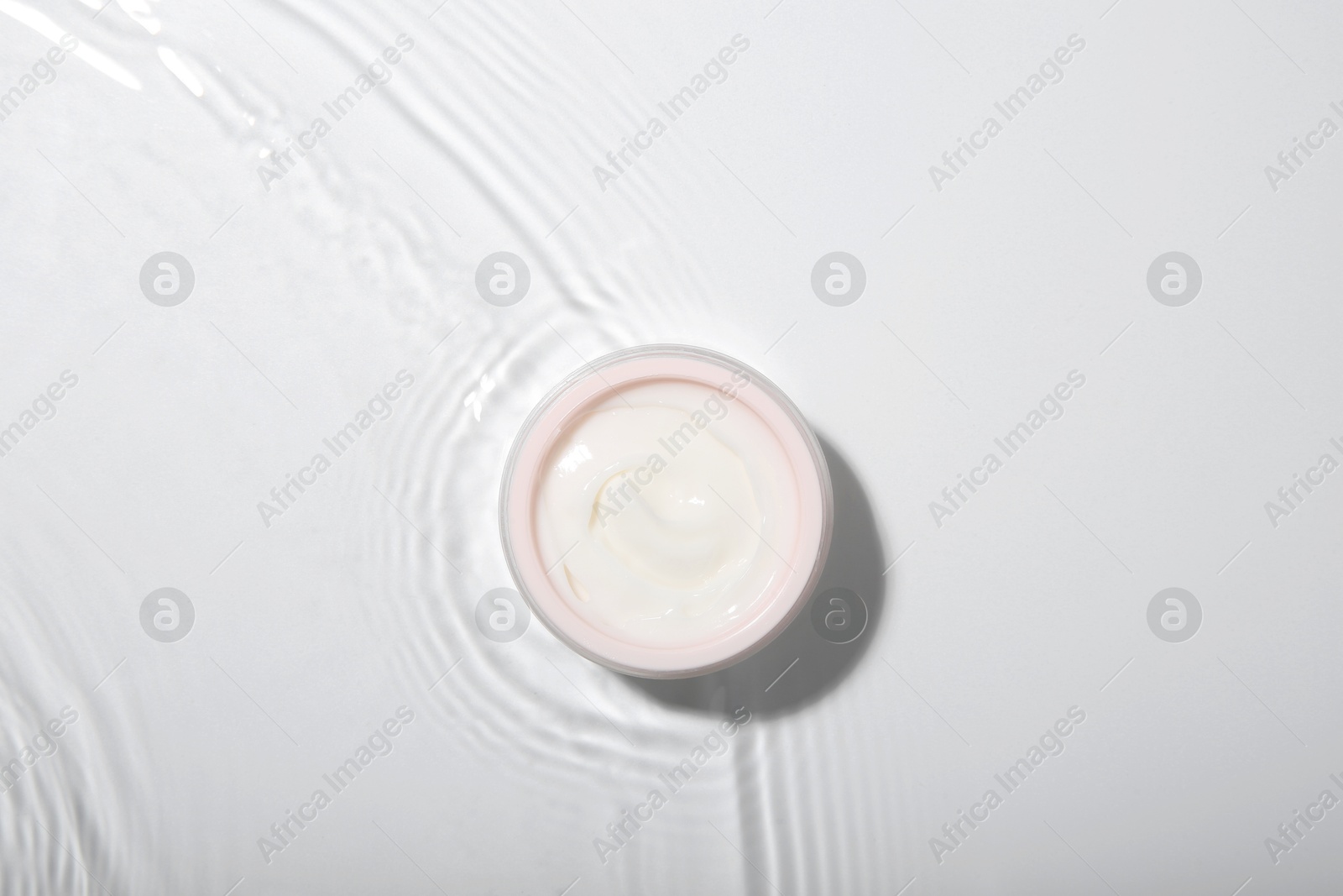 Photo of Cosmetic product. Jar with cream in water on light background, top view