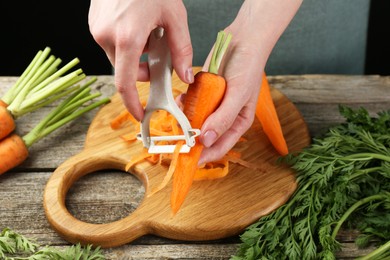 Woman peeling fresh carrot at wooden table, closeup