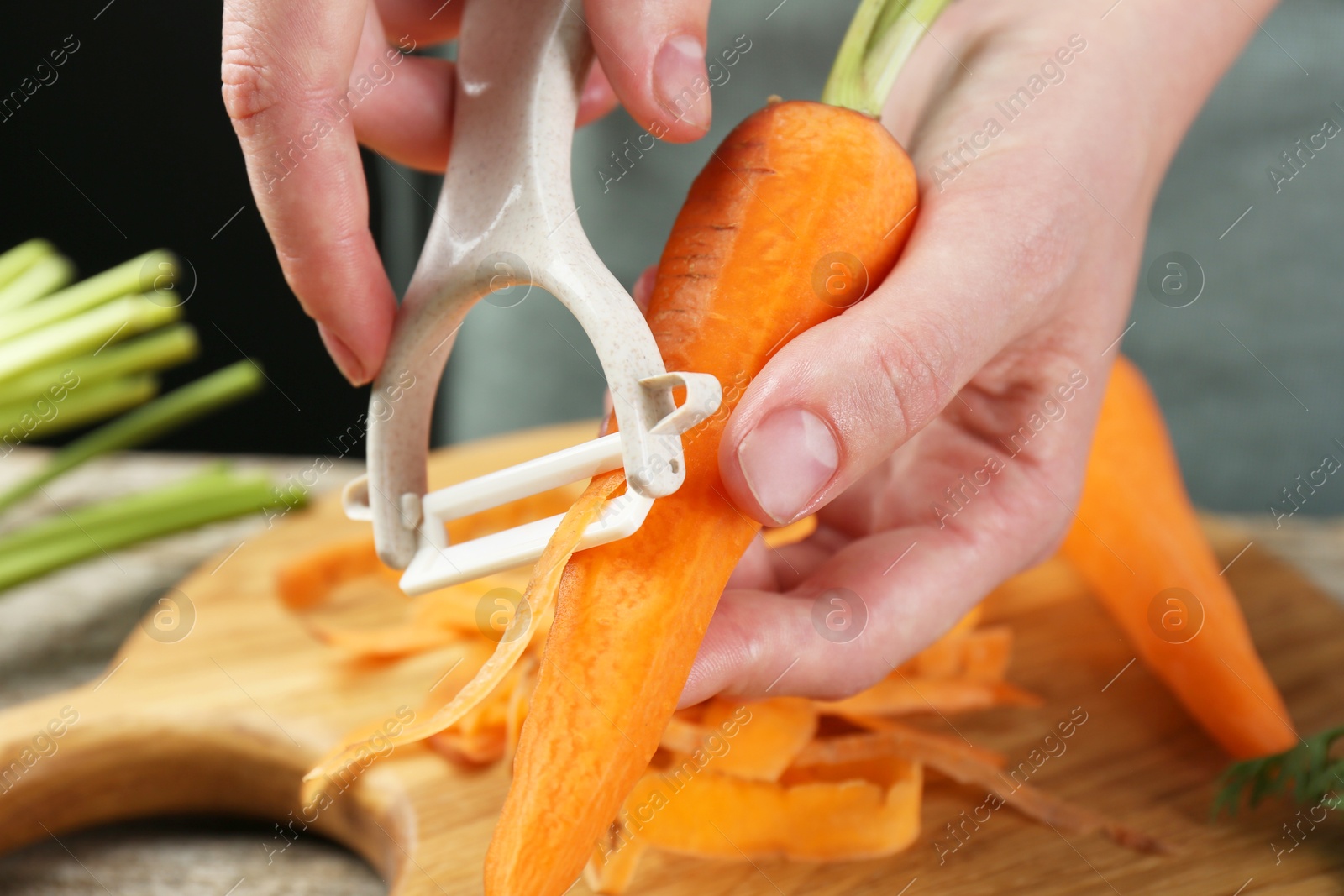 Photo of Woman peeling fresh carrot at wooden table, closeup