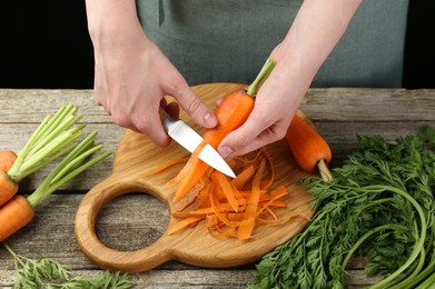 Photo of Woman peeling fresh carrot with knife at wooden table, closeup